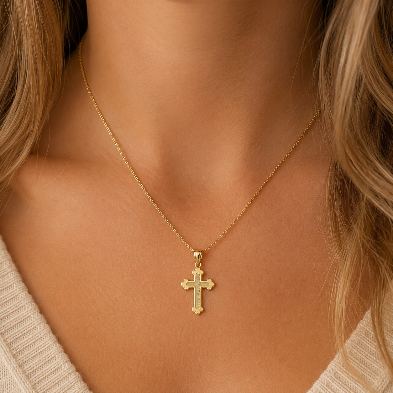 [group: large]A close-up of a woman's neck and chest wearing a delicate gold cross pendant necklace on a fine chain.