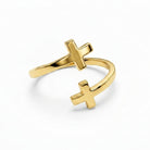 A polished gold open cuff ring featuring two distinct cross motifs, one larger and one smaller, set against a seamless white background.