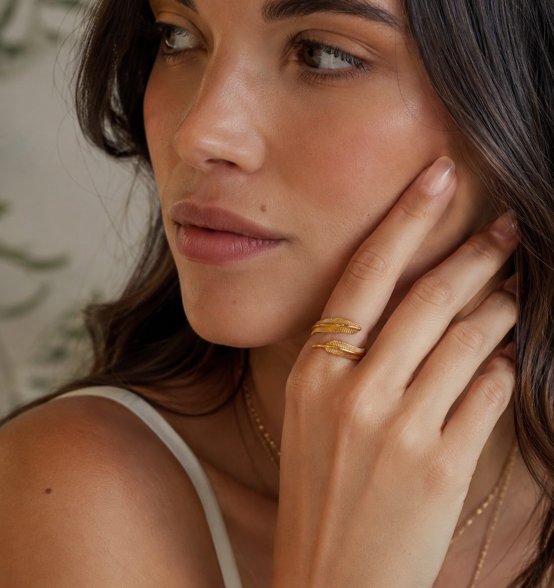 Woman wearing gold rings and a necklace, with one hand near her face.
