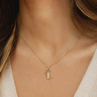 A close-up of a model's neck and chest wearing a delicate gold chain necklace with a small boot-shaped pendant featuring a silver-colored accent.
