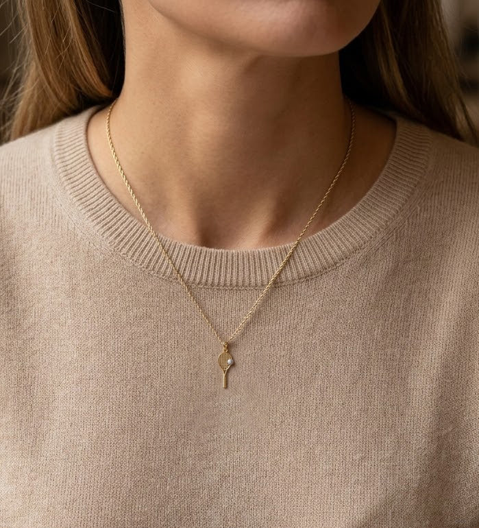 Gold necklace with a tennis pendant worn by a person in a beige sweater.