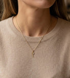Gold necklace with a tennis pendant worn by a person in a beige sweater.