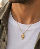 [group: gp] A close-up of a man's neck and chest wearing a gold chain necklace with a textured leaf pendant containing a small clear gemstone, styled over a white t-shirt and an olive green button-up shirt.