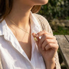 Person wearing a gold necklace with a small soccer ball pendant outdoors