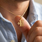 [group:10k-gold] Gold necklace with '#1 Dad' pendant held by a person wearing a light blue shirt.