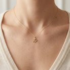 A delicate gold chain necklace with a small floral pendant worn on a model's neck, paired with a cream-colored knit top.