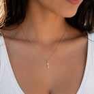 A close-up lifestyle shot of a model wearing a delicate gold chain necklace with a small key-shaped pendant, styled with a white ribbed top.