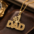 [group:10k-gold]  Gold #1 DAD pendant on a brown leather surface with a watch in the background