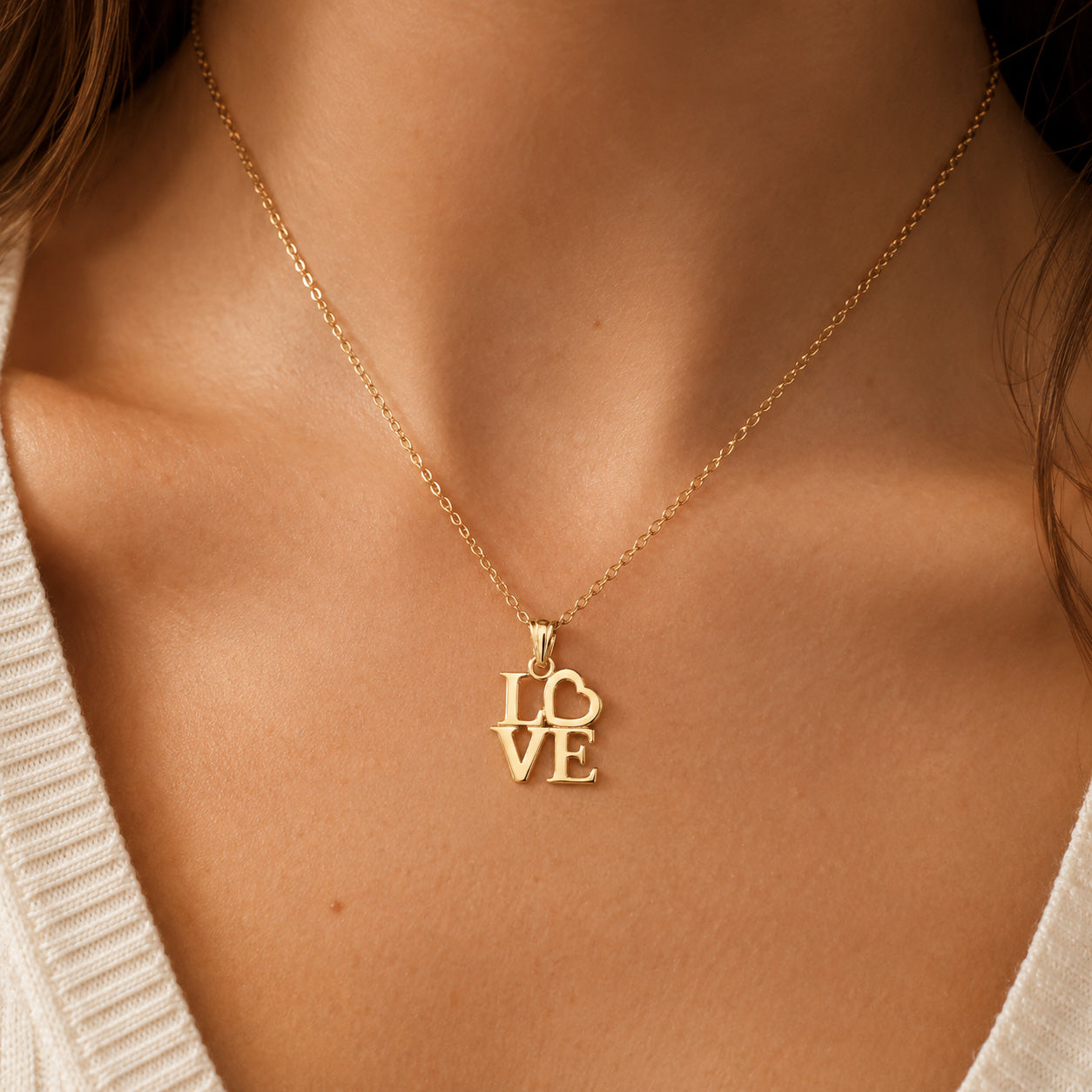 [group: gold-plated]A close-up of a person's neck and chest wearing a delicate gold chain necklace with a pendant spelling 'LOVE' in stacked letters.