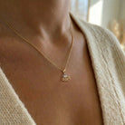 A close-up of a person wearing a delicate gold chain necklace with a small script pendant spelling 'Queen', styled with a cream knit cardigan.